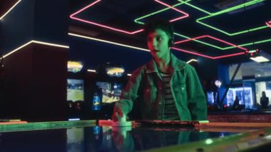 Kot ceketli, kulaklıklı, 80 'lerin retro atari salonunda arkadaşıyla hokey oynarken hafta sonları eğlenen odaklanmış genç bir çocuğun orta boy fotoğrafı.