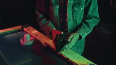 Oyun makinelerinde, hava hokeyi masasının yanında duran, retro çalgıcıya kaset takan, müzik dinleyen ve favori melodiyi dinleyen genç bir çocuğun orta ölçekli yakın çekimi.