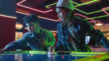 Neon ışıkta, neon ışıkta, iki farklı genç arkadaştan oluşan bir takımın hava hokeyi oynadığı orta ölçekli bir çekim. Umutsuzca tepki veriyor, gülüyor ve devam ediyor.