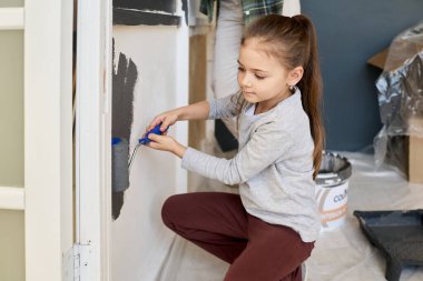 Annesinin yeni dairesini yenilemesine yardım ederken, oturma odasının duvarını gri renklerle boyayan tatlı bir kız.