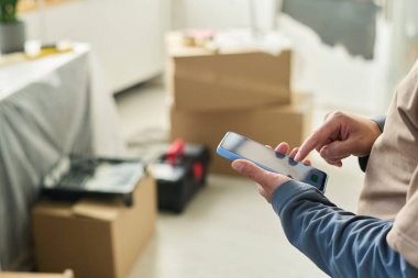 Oturma odasında kameranın önünde dururken cep telefonu ekranını işaret eden tanınmamış genç adamın eli.