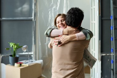 Bej rengi pamuklu genç bir adamın mutlu karısını kucaklayıp elinde yeni evlerinin anahtarlarıyla...