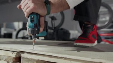 Kırmızı spor ayakkabılı, tahta paleti delen, elektrikli matkap kullanan, BMX sürmek için ahşap rampa parçaları birleştiren isimsiz bir adamın elleri.