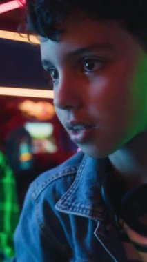 Oyun salonunda oyun oynayan iki genç arkadaşın orta boy dikey görüntüsü. Rakiplerine karşı sakız çiğneyen Asyalı çocuk. Kafkasyalı şapkalı çocuğa beşlik çakıyor.