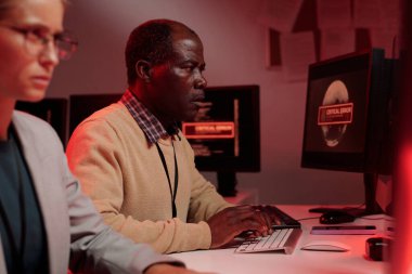 Olgun Afro-Amerikan erkek bilişim yöneticisi, iş yerinde teknik sorunu çözmeye çalışırken bilgisayarın tuşlarına basıyor.