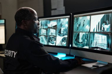 Ciddi güvenlik görevlileri birkaç masaüstü bilgisayar ekranına bakarken güvenlik kamerası görüntülerine konsantre oluyor.