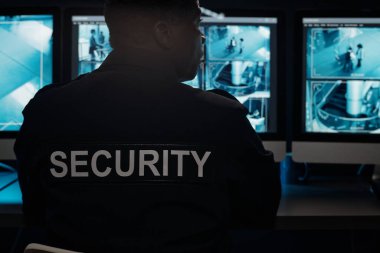 Modern güvenlik görevlisi siyah üniformalı, oteldeki güvenlik kamerası görüntülerini izlerken kameranın önünde oturuyor.