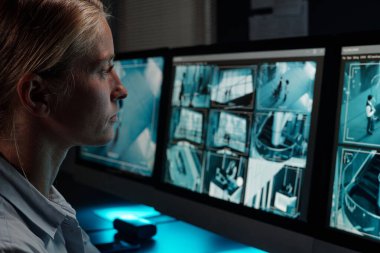 İş yerinde çalışan genç ve ciddi bir bayan gardiyan kameranın önünde oturup kapalı devre televizyon videolarıyla bilgisayar ekranına bakıyor.