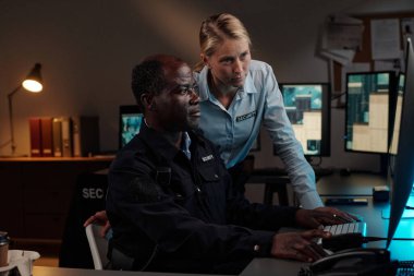 Genç bayan güvenlik görevlisi, yetişkin bir erkek Afrikalı Amerikalı meslektaşın yanında, ikisi de güvenlik kamerası görüntülerini izliyordu.