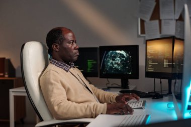 Ciddi bir Afro-Amerikan bilişim yöneticisi veya programcı iş yerinde otururken masaüstü bilgisayar ekranında veri çözüyor