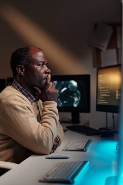 Dalgın Afrikalı Amerikalı erkek programcı parmaklarını ağızdan tutuyor ve veriyi çözmeye çalışırken bilgisayar ekranına bakıyor.