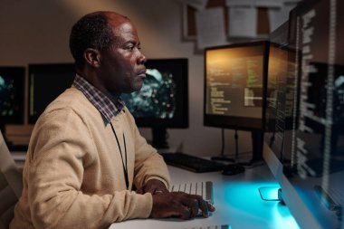 Ciddi erkek bilişim mühendisi, ofiste yeni yazılımlar geliştirirken elini bilgisayar faresinin üzerinde tutuyor ve ekrana bakıyor.