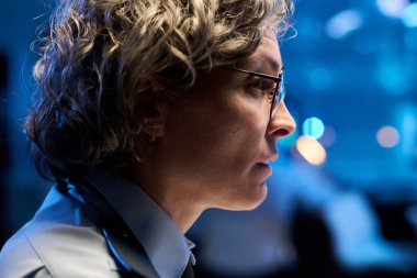 Gözlüklü, gri saçlı kadın memurun profili kameranın önündeki verilerle bilgisayar ekranına bakıyor.