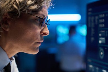 Masaüstü bilgisayar ekranındaki grafik verilerine dikkatle bakan, gözlüklü, olgun, ciddi kadın operatörün yan görüntüsü