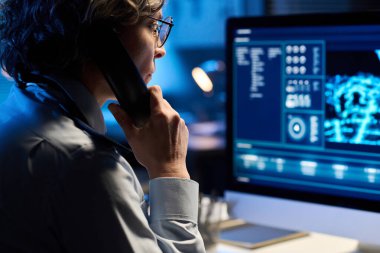 Üniformalı olgun bir kadına odaklan telefon ahizesini kulağından tut ve durumu bildirirken bilgisayar ekranına bak.