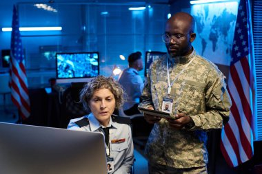 Genç Afrikalı Amerikalı erkek subay ve olgun bayan meslektaşı masaüstü bilgisayar ekranında grafik verilerini tartışıyorlar.