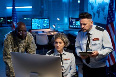 Üniformalı üç ciddi kültürler arası memur askeri komuta merkezindeki bilgisayar ekranındaki çevrimiçi verilere bakıyor.