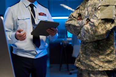 Askeri bilgiler tartışılırken iki tanınmayan üniformalı erkek subay kameranın önünde dikiliyor.