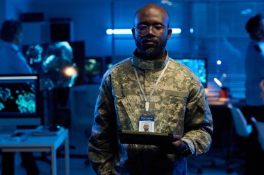 Askeri komuta merkezinde çalışırken tablet ekranlara bakan kamuflaj üniformalı ciddi bir Afrikalı Amerikalı.