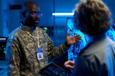 Kamuflaj üniformalı kendinden emin Afro-Amerikan adam tartışma sırasında ordunun konumuyla etkileşimli ekranı işaret ediyor.