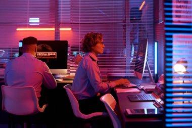 Üniformalı, bilgisayar monitörünün önünde oturan ve tuş takımına yazı yazan ciddi bir kadın memurun yan görüntüsü