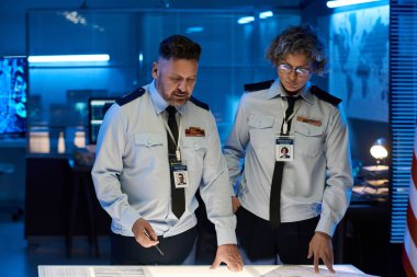 Askeri komuta merkezinin iki yetişkin erkek ve kadın subayı masadaki kağıt belgelere bakıyor ve onları tartışıyor.