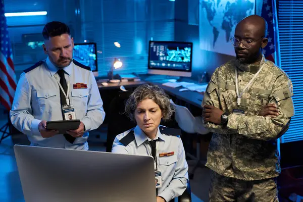 Ciddi, olgun bir kadın ve iki kültürler arası meslektaşı masaüstü bilgisayar ekranına bakıyor.