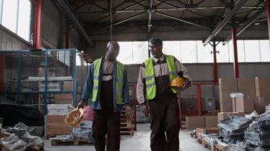 Orta boy erkek depo çalışanları, Asyalı denetçi ve Afro-Amerikan mühendis, üniforma, şapka, sarı yelek, depolama alanlarını denetleme, operasyon konularını tartışmalar.