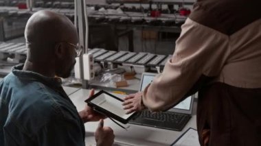 Bilinmeyen erkek fabrika ürün mühendisinin Afrika kökenli Amerikalı yöneticiye LED lamba özelliklerini açıklarken, yeni müşteri siparişini tartışırken ve dizüstü bilgisayardaki örneğe bakarken orta boy arka planı.