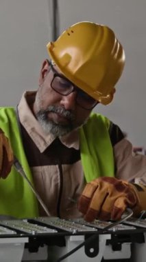 Orta yaşlı Hintli erkek montaj hattının dikey yakın plan portresi sarı başlık uzmanı ürün bileşenlerinden döküntüleri atıyor, aracı indiriyor, kameraya bakıyor, güvenle gülümsüyor.