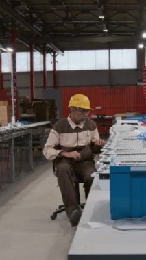 Geniş atölyedeki iki farklı ışık fabrikası uzmanının tam dikey çekimleri, sandalyede dönen Asyalı erkek işçi, müşteri siparişini yerine getirmek için teknik çizimleri kontrol eden siyah mühendis.