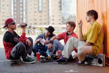 Bir grup arkadaş canlı bir şekilde dışarıda oturmuş sohbet ediyor, arkadaşlığın tadını çıkarıyor ve canlı şehir arkaplanının etrafında birlikte eğleniyorlar.