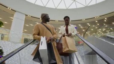 Alışveriş merkezinde başarılı bir alışveriş yaptıktan sonra yürüyen merdivenden inerken gülümseyen Afrikalı genç çiftin düşük açılı görüntüsü.