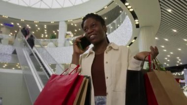 Haftasonu mağazada akıllı telefondan konuşurken elinde bir sürü alışveriş torbası tutan ve gülümseyen şık Afro-Amerikan kadınlarının orta açılı çekimi.