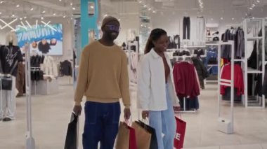 Mutlu Afro-Amerikan eşleri mağazadan bir sürü kese kağıdıyla çıkıyorlar ve gülümsüyorlar, alışveriş merkezinde alışveriş yaparken birlikte eğleniyorlar.