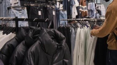Kıyafetçiden süveter ve kalın ceketler seçen tanınmayan erkek müşterinin orta bölüm kesimi.
