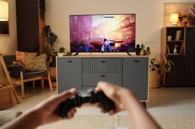 Sıcak dekore edilmiş bir oturma odasında, bir eğlence merkezini çevreleyen rahat oturaklı ve bitkilerle TV 'de video oyunu oynarken el ele tutuşan oyun kontrolörü.