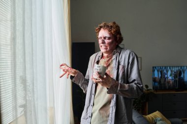 Oturma odasında dikilirken pencereden dışarı bakan kızgın erkek zombi resmi.