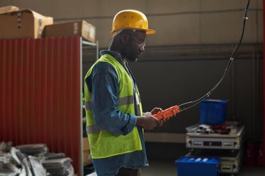 Depoda endüstriyel ekipmanlarla çalışırken kontrol panelinde düğmelere basan Afrikalı Amerikalı fabrika işçisinin yan görüntüsü