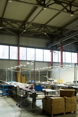 Modern fabrikanın geniş atölyesinde yeni ürünler üretmek için çeşitli çalışma ekipmanlarıyla dolu uzun masalar.