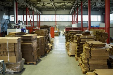 Modern fabrika deposunda duran ahşap paletlerin üzerinde duran iki sıra karton çarşafın arasında uzun koridor.