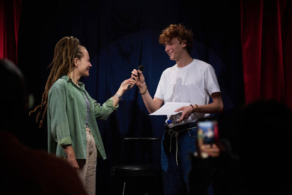 Два человека, участвующих во взаимодействии на сцене, с одним человеком, передающим микрофон другому, который читает из газеты