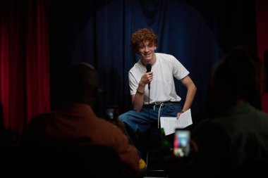 Comedian in white shirt joyfully delivering a stand-up performance on stage Holding mic in hand, engaging with audience, creating lively atmosphere clipart