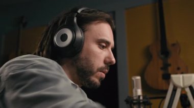 Rastalı, kulaklık takan, stüdyoda yeni müzik yapan, arka planda bulanık arka planda mikrofon ve elektro gitar çalan meşgul genç erkek söz yazarının yüzünü kapatıyoruz.