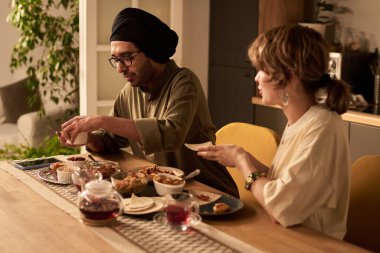 İki kişi yemek masasında oturmuş, sıcak aydınlatma altında Asya yemeklerinin tadını çıkarıyor, rahat bir akşam yemeği sohbetine girişiyor.