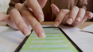Masasında oturan, akıllı telefondaki bütçe planlama uygulamasını kullanan, masraf tiplerini yazan ve aylık giderleri hesaplayan isimsiz genç kadının ellerini kapat.