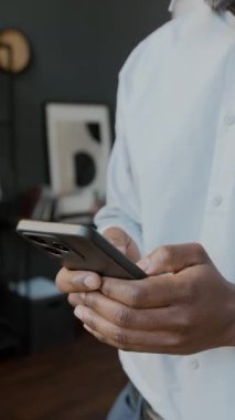 Ofiste beyaz gömlekli, iş günü akıllı telefonunda mesaj ya da e-posta yazan tanınmayan siyah şirket yöneticisinin elleri dikey olarak kapanır.