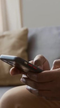 Evdeki kanepede oturan, arkadaşlarıyla sosyal medyada iletişim kurarken akıllı telefondan mesajlar yazan isimsiz siyahi adamın elleri dikey olarak kapanır.