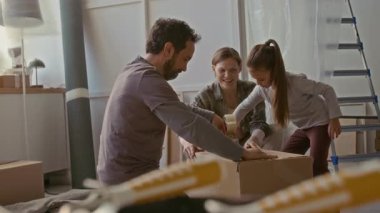 Mutlu genç ebeveynler ve şirin küçük kızları birbirlerine beşlik çakıyor. Ev eşyaları yapıştırıcı bantla mühürlenip yeniden yapılanmaya hazırlanıyor.
