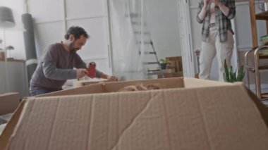 Karton kutudan ailesinin eşyalarını paketlemesine ve taşınma sırasında kızının fotoğrafını çekmesine rağmen kameraya bakan sevimli küçük kız.